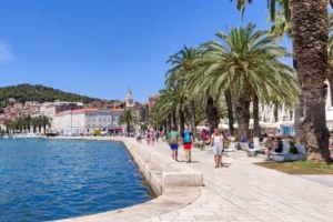 People walking along a seaside promenade in Split, Croatia, with historic buildings and the Adriatic Sea in the background