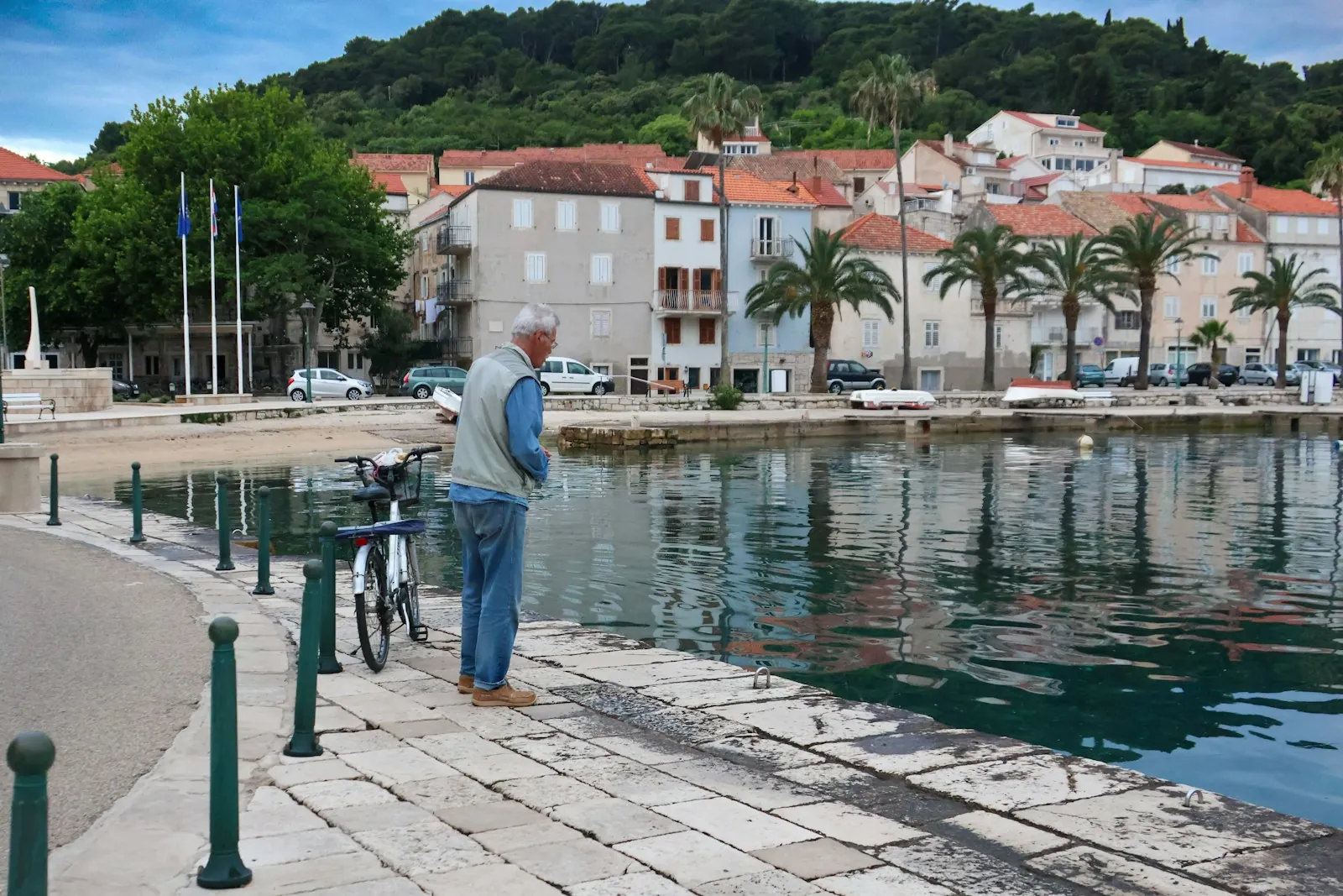croatia-coastal-town-waterfront-man Old man standing by the sea in Croatian coastal island town with boats and traditional houses in the background