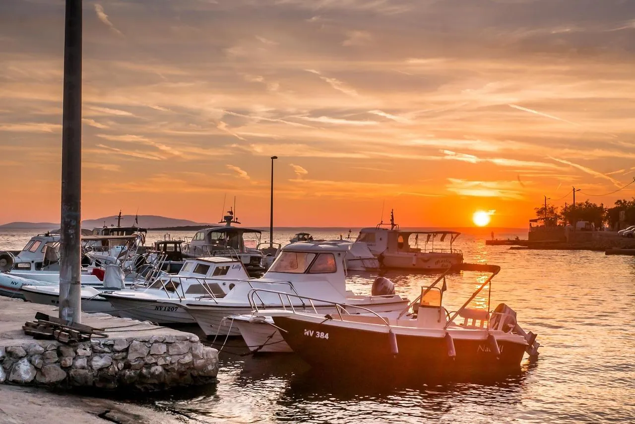 Sunset over the coastline of Pag Island, Croatia, with boats moored near the shore and warm evening light