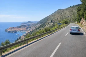 View of Dubrovnik from the coastal D8 road with a car driving towards the city, part of the Dubrovnik transport guide 2026