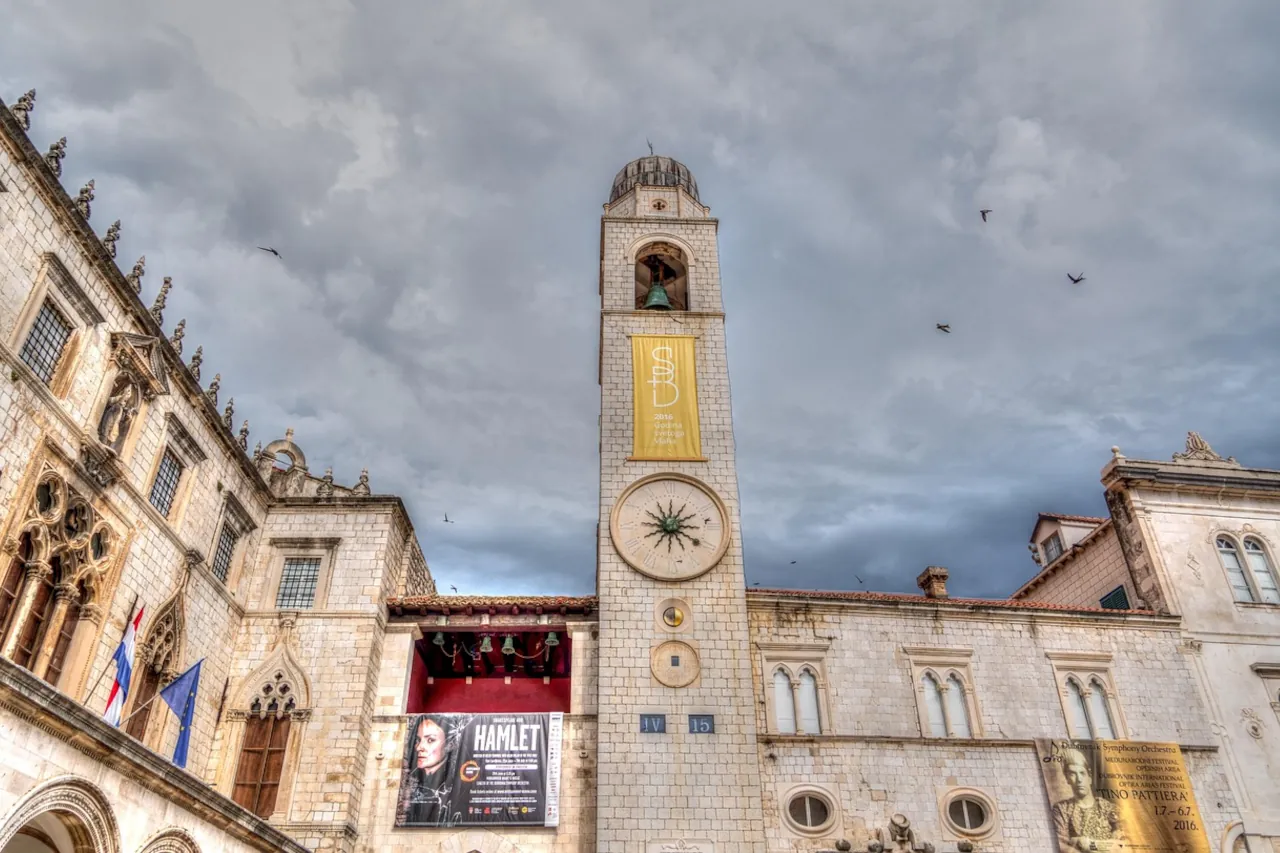 Stradun clock tower in Dubrovnik with dramatic cloudy sky and changing weather