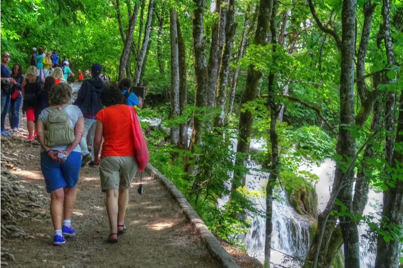 plitvice-lakes-croatia-walking-trail-tourist-group Tourists walking along a forest trail next to waterfalls at Plitvice Lakes in Croatia