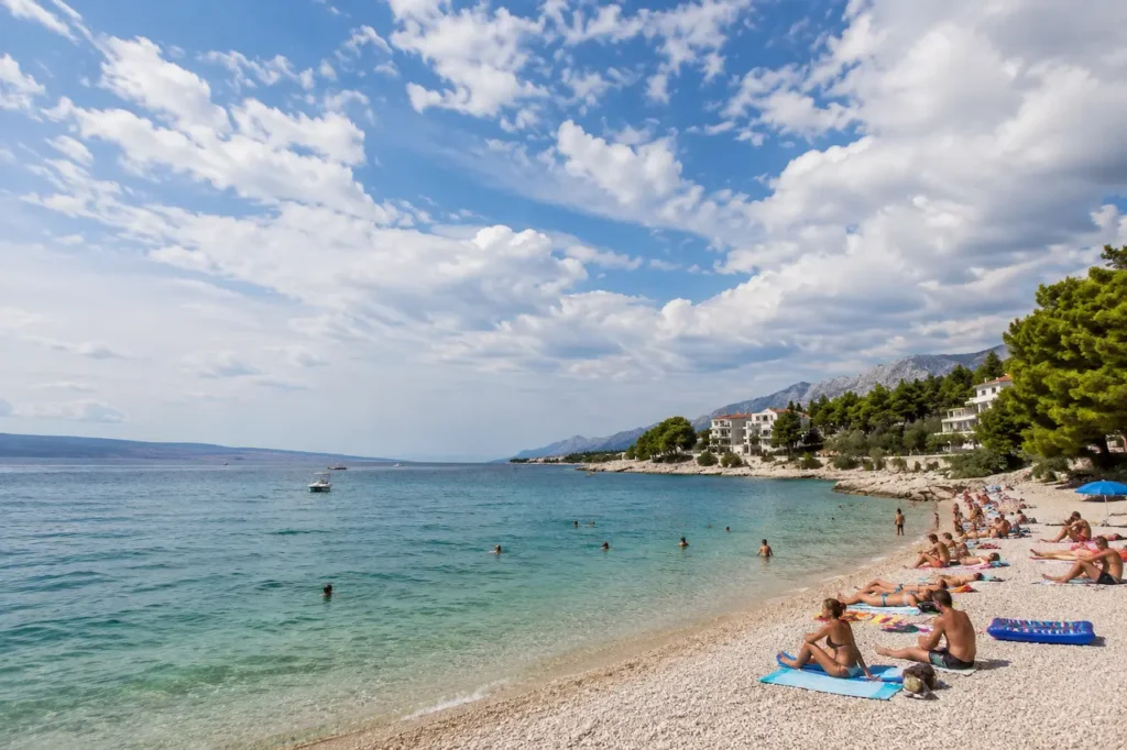 Weather in Croatia on a sunny Adriatic beach with swimmers and clouds over the coast