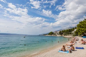Weather in Croatia on a sunny Adriatic beach with swimmers and clouds over the coast
