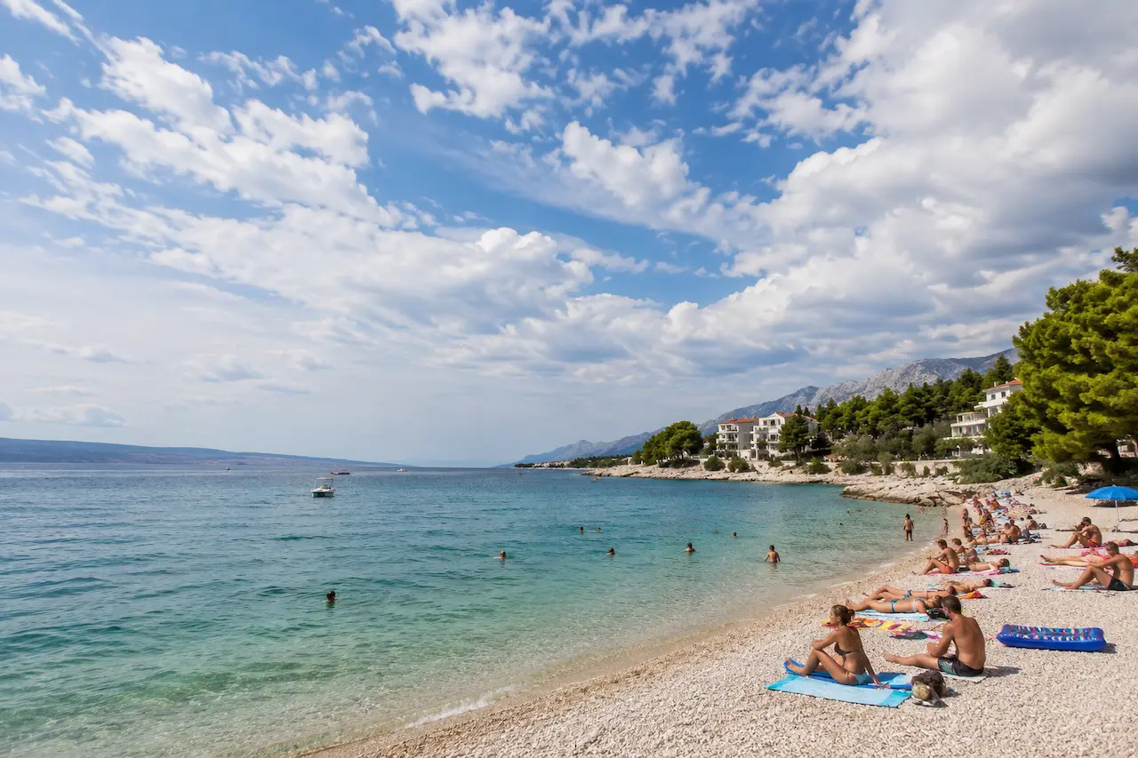 Weather in Croatia on a sunny Adriatic beach with swimmers and clouds over the coast