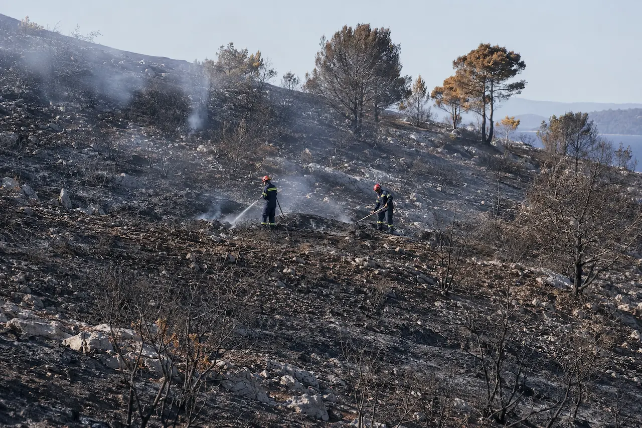 Two firefighters carrying out mop-up work on a burned Adriatic hillside, illustrating tougher arson penalties under the new ecocide law in Croatia.