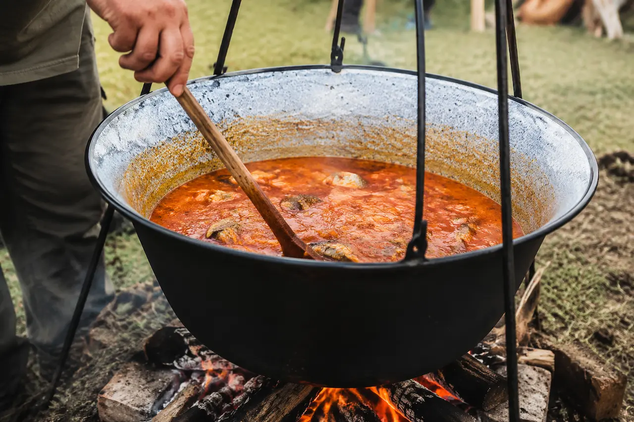 A cook stirring fiš paprikaš in a cauldron over an open fire at a Croatian fish stew festival in Baranja.